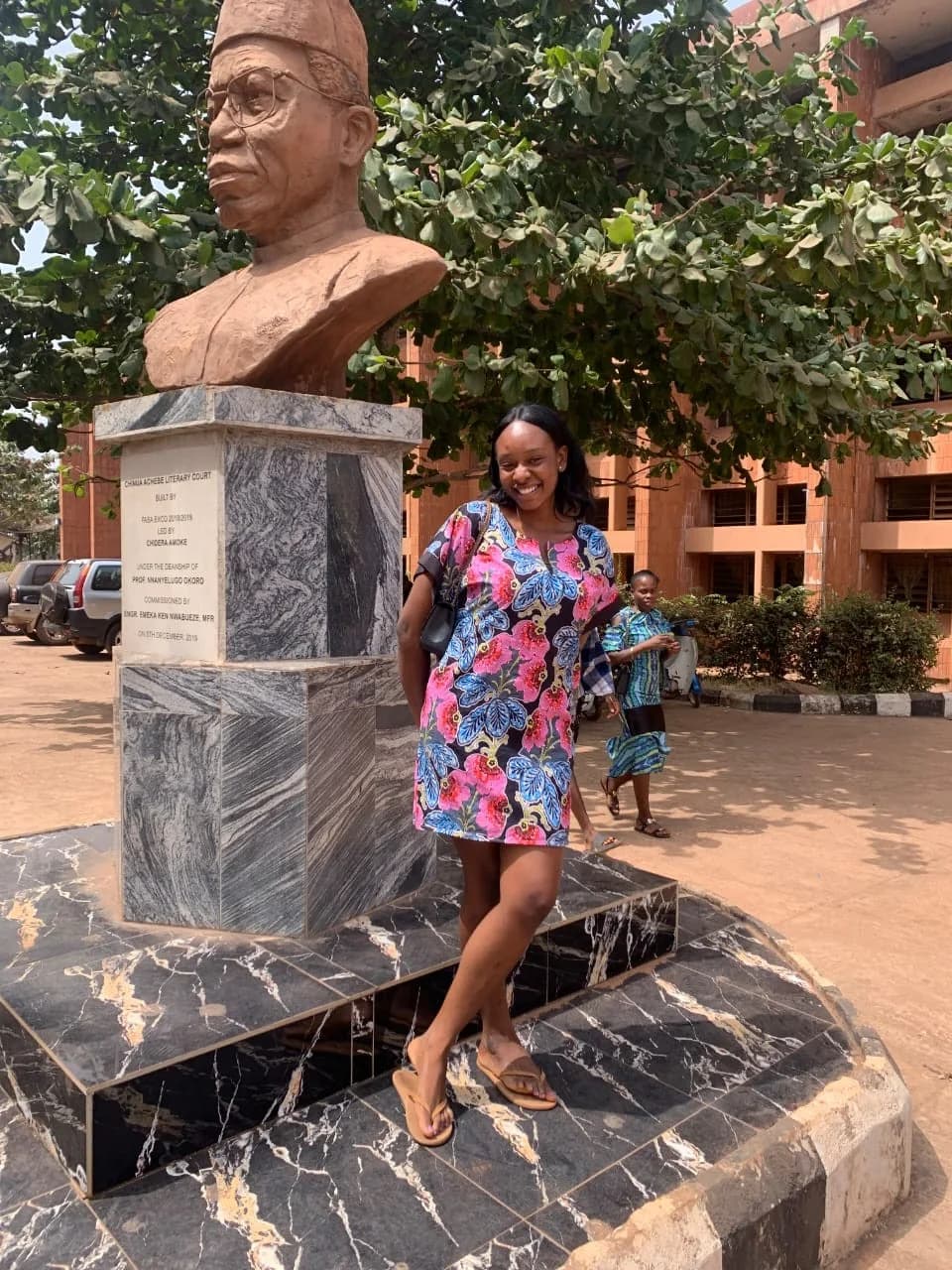Peace in a floral dress beside a bust on the UNN campus
