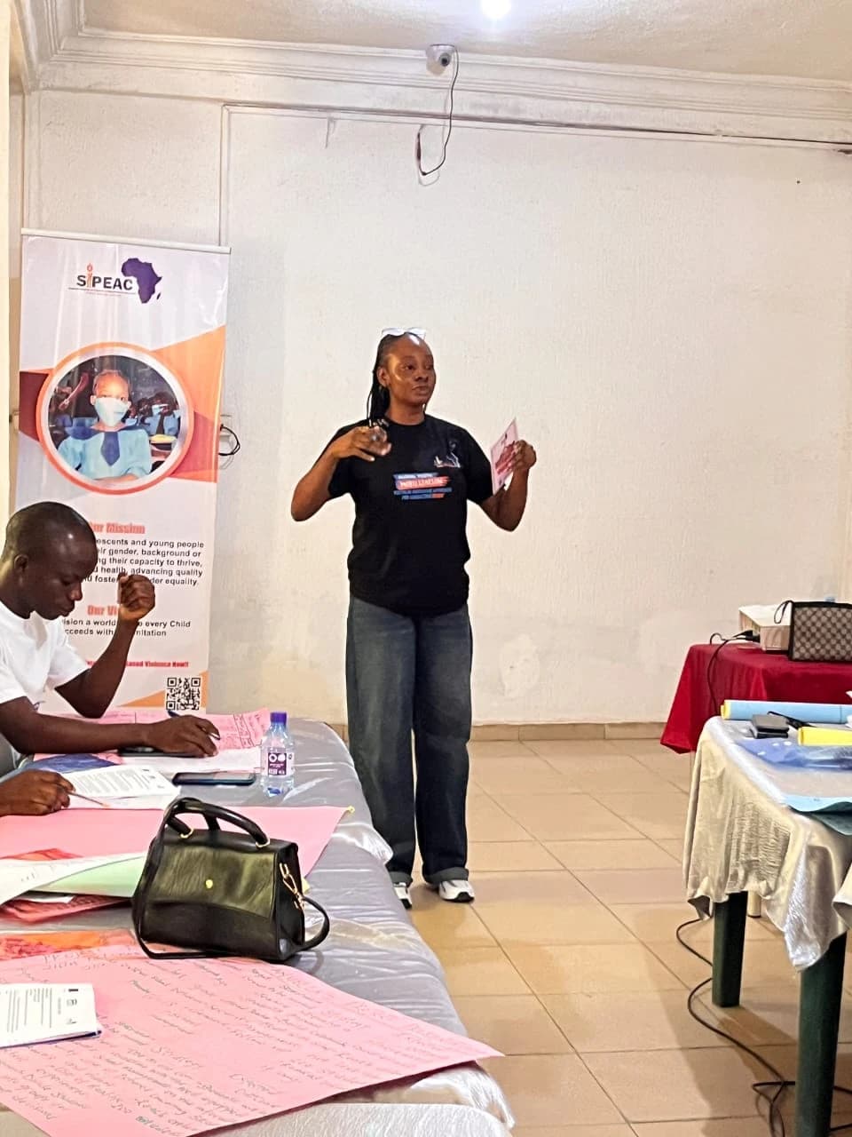 Peace facilitating a SIPEAC session beside the SIPEAC banner